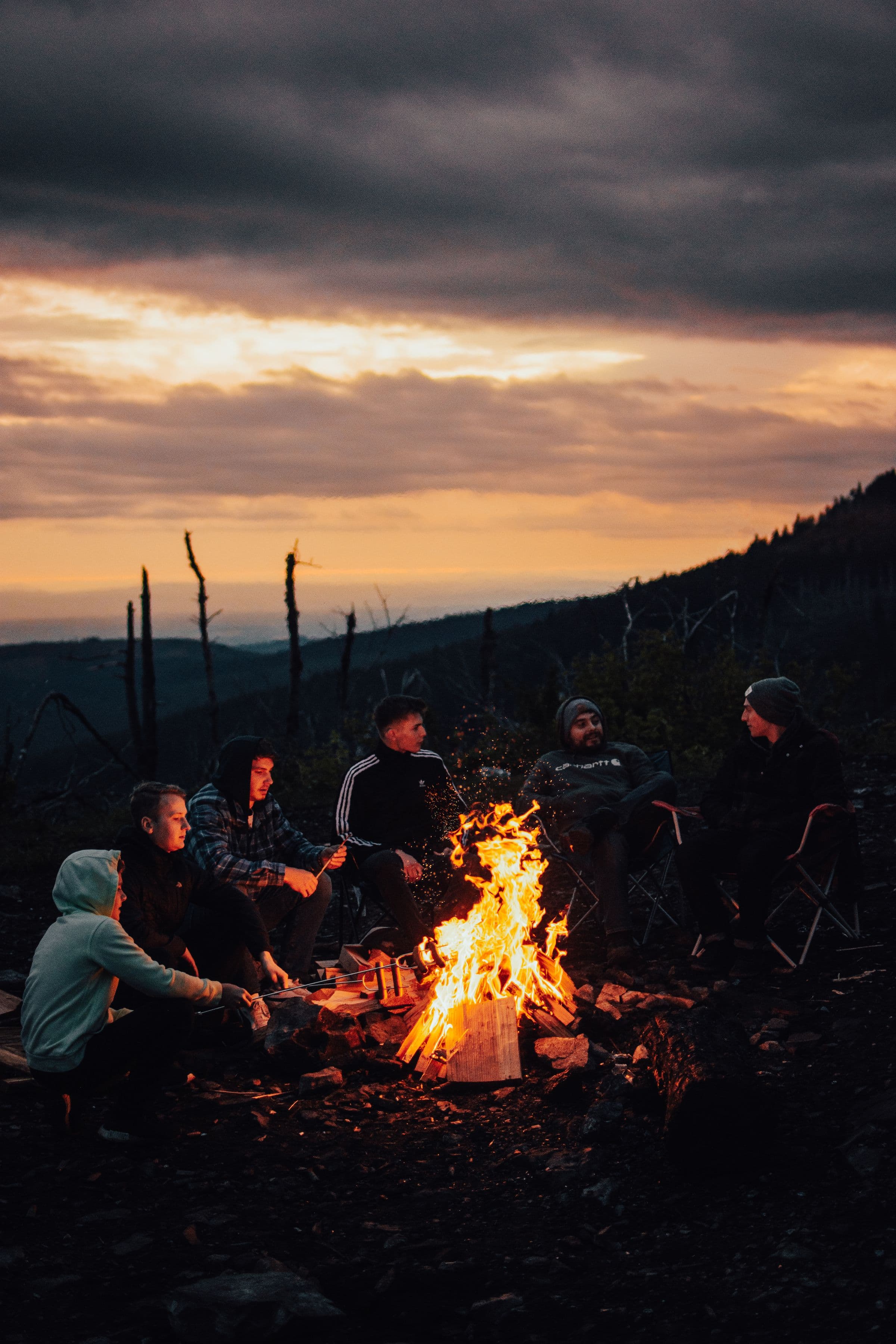 Friends gathered around a campfire at dusk on a ridge