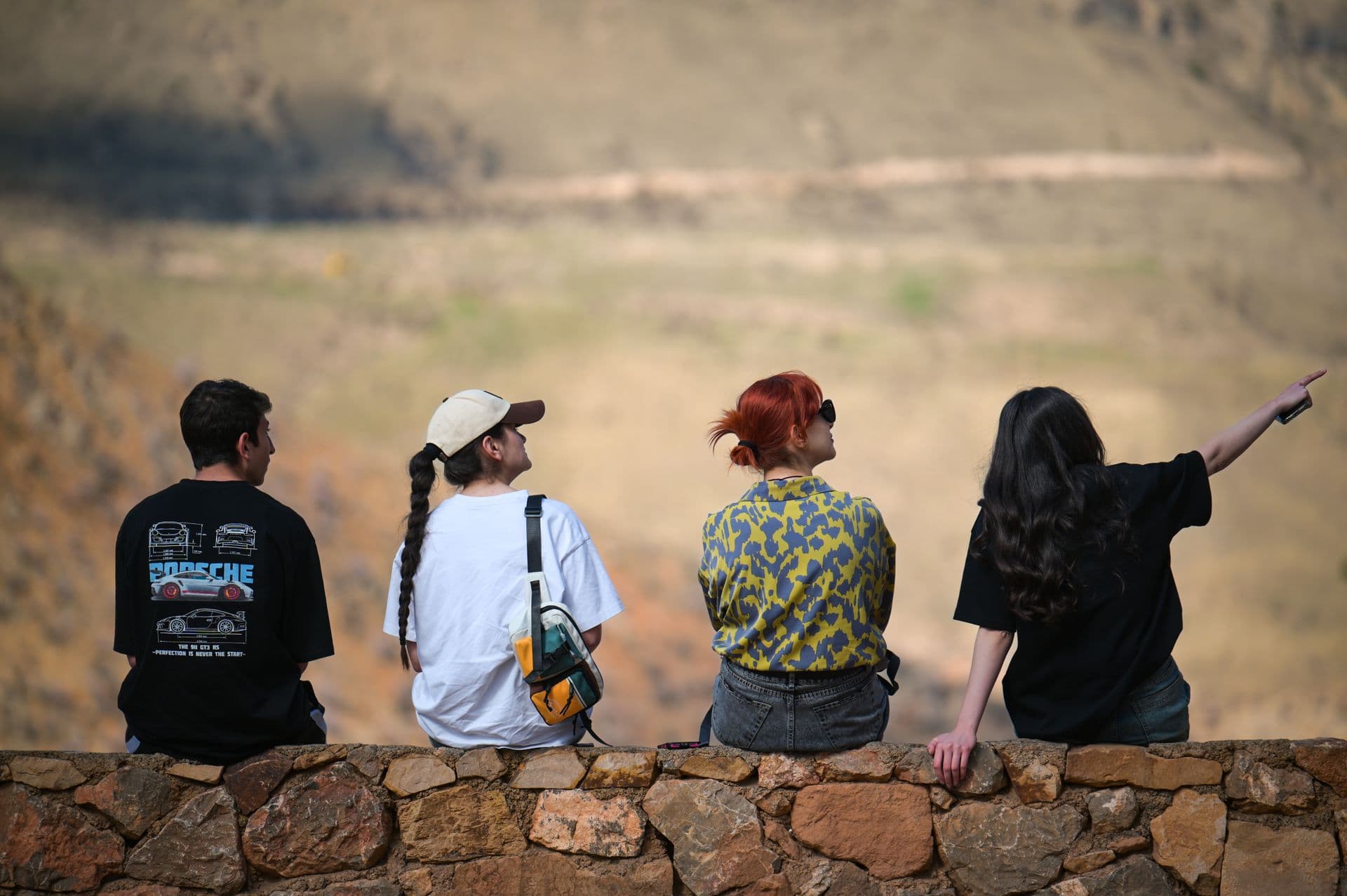 Friends on a stone wall pointing out a valley view