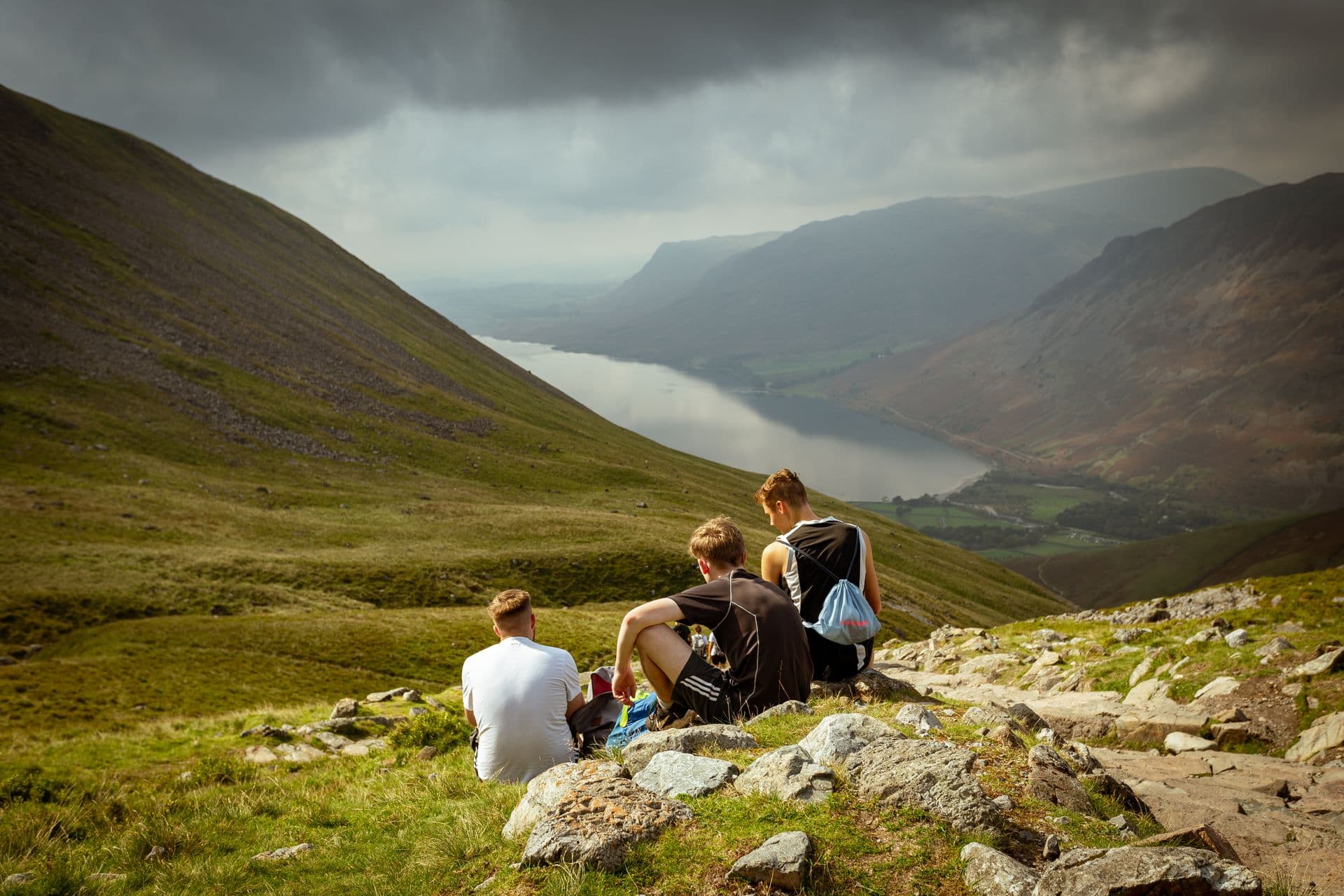 Friends sitting together on a grassy ridge above a valley lake