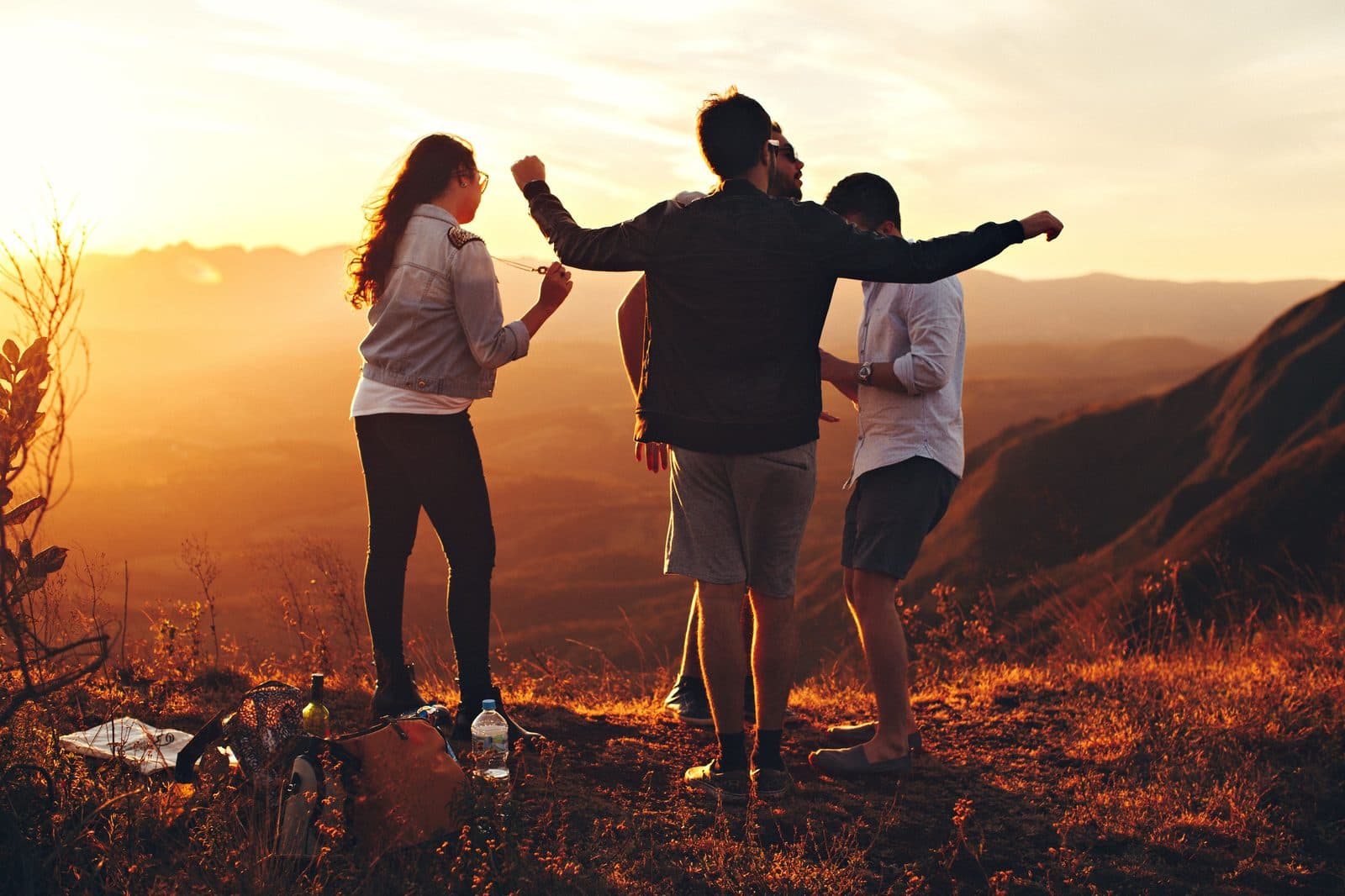 Friends cheering with arms raised at golden hour on a ridge