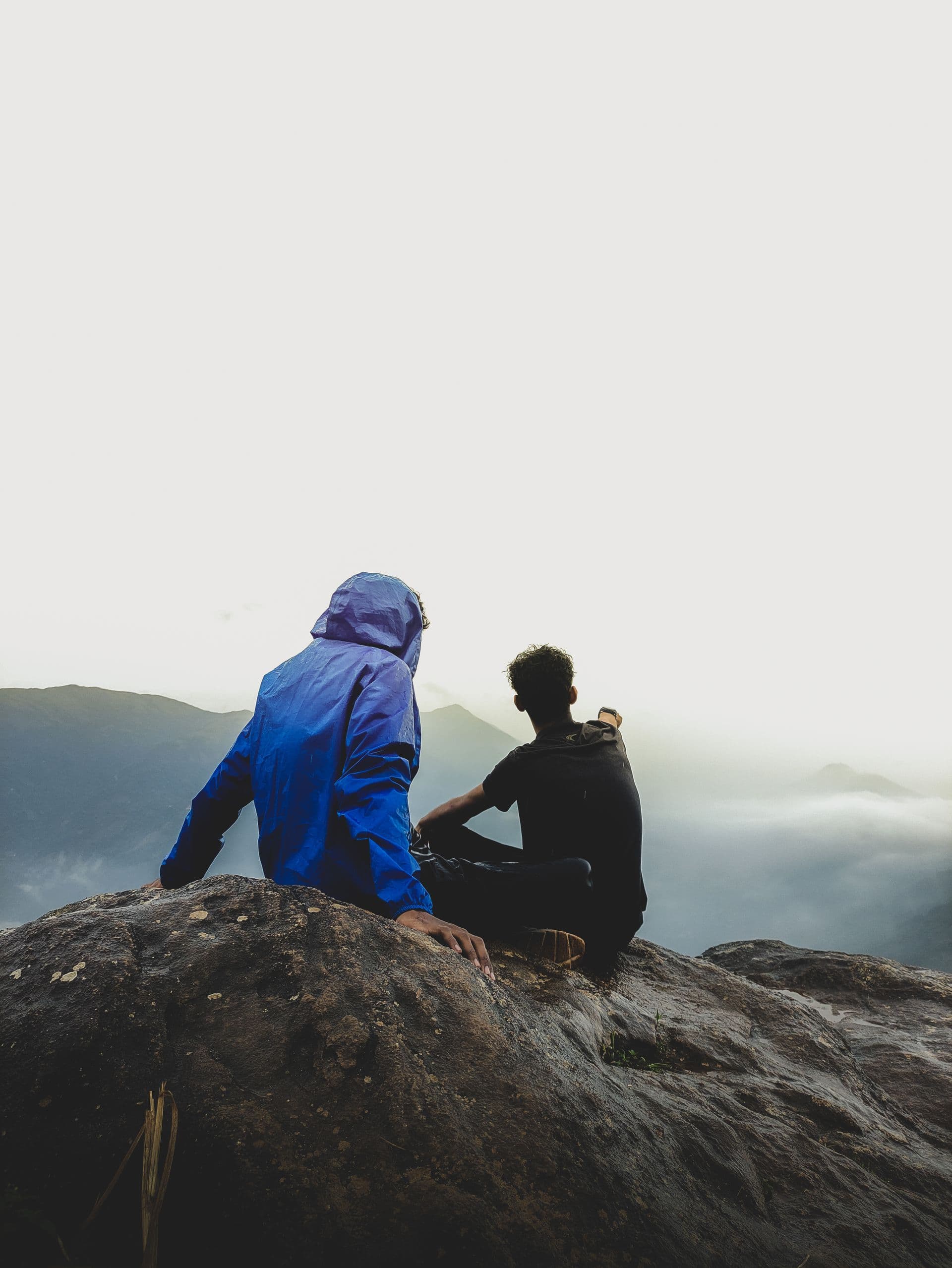Two friends sitting on a rock looking into the mountain mist
