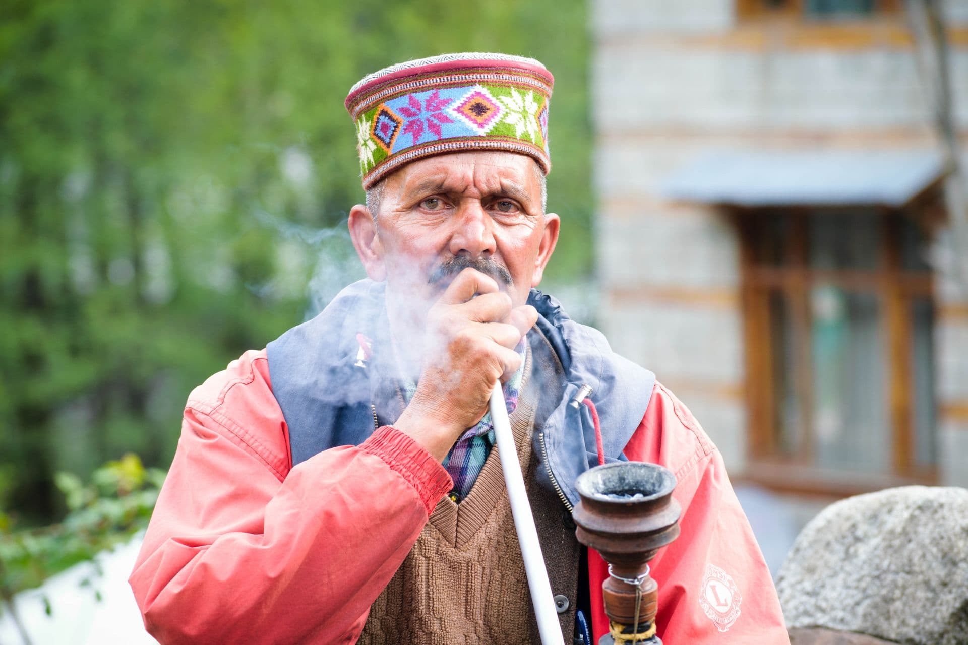 A Kullu elder in a traditional cap smoking a hookah
